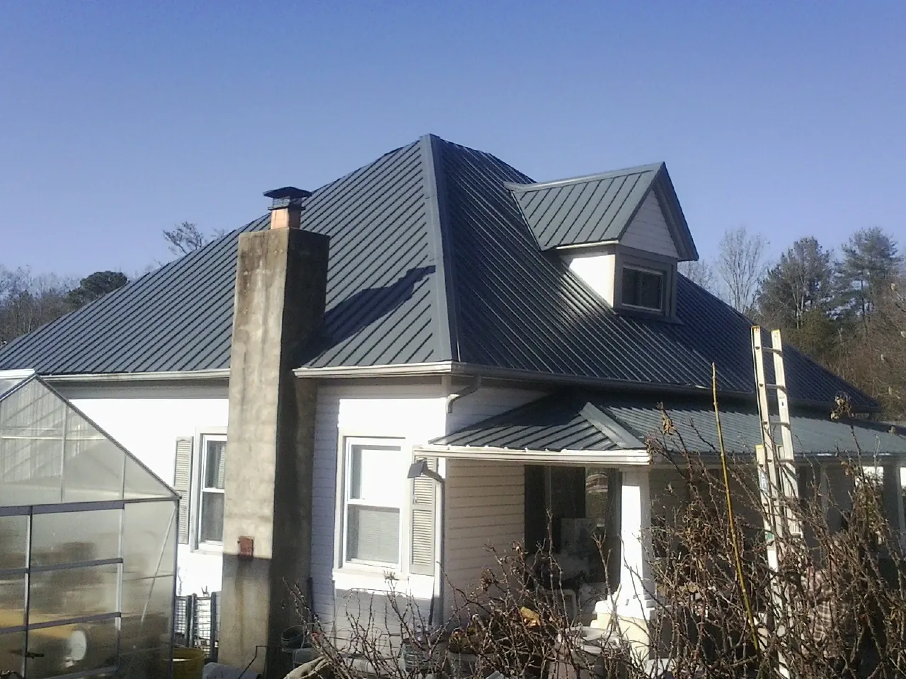 Dark blue standing seam metal roof on a white farmhouse with dormer — Slate & Tile Roof Repair by Roofing Brothers in Hayward