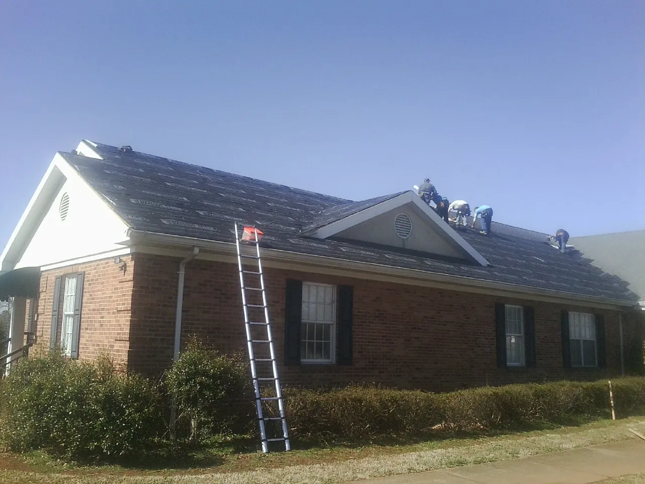 Crew tearing shingles off a brick ranch roof with a ladder set — Metal Roof Repair work by our crew in Hayward