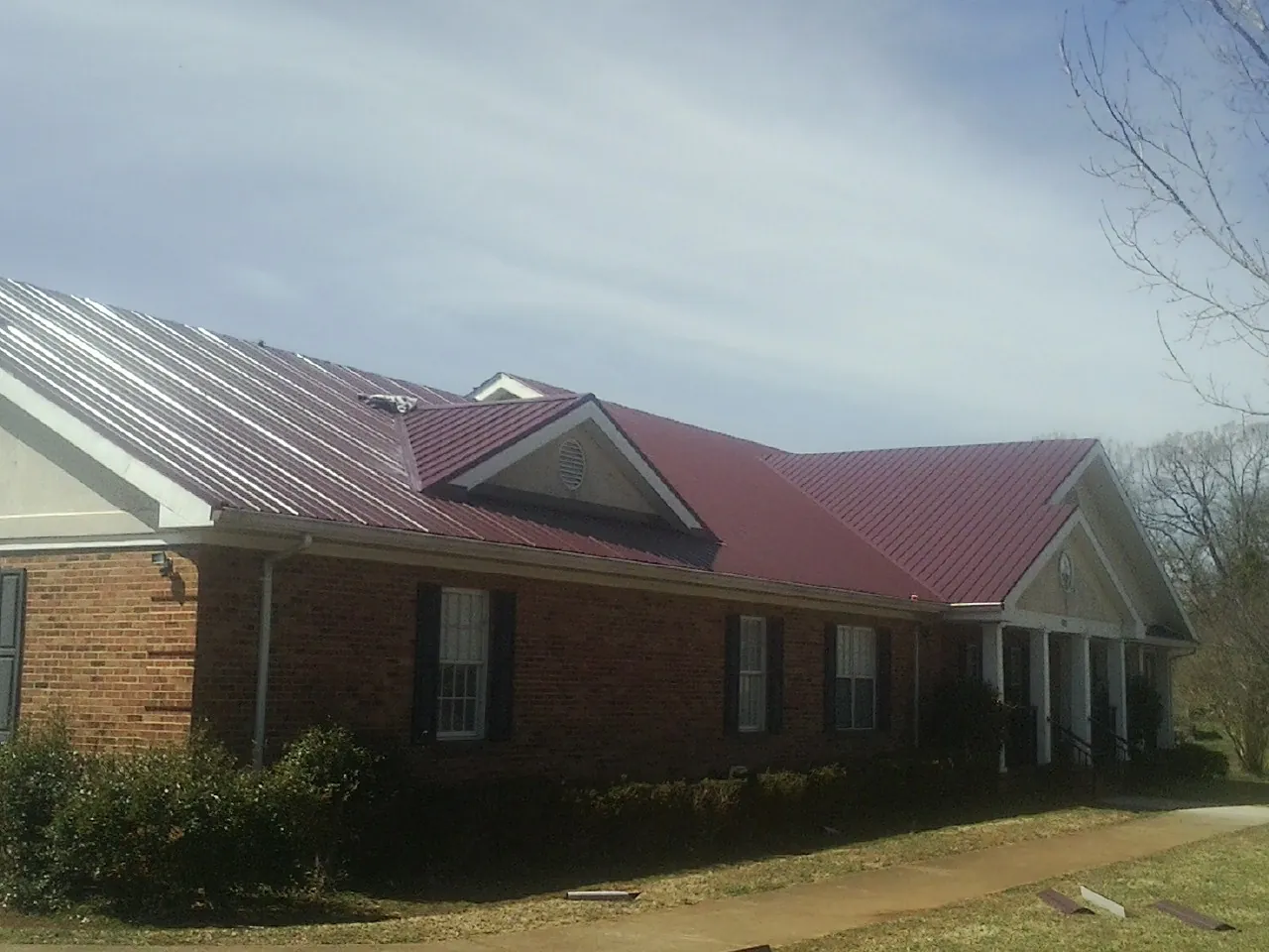 Red metal roof with gabled entries on a long brick building, from a Hail Damage Roof Repair job in Hayward
