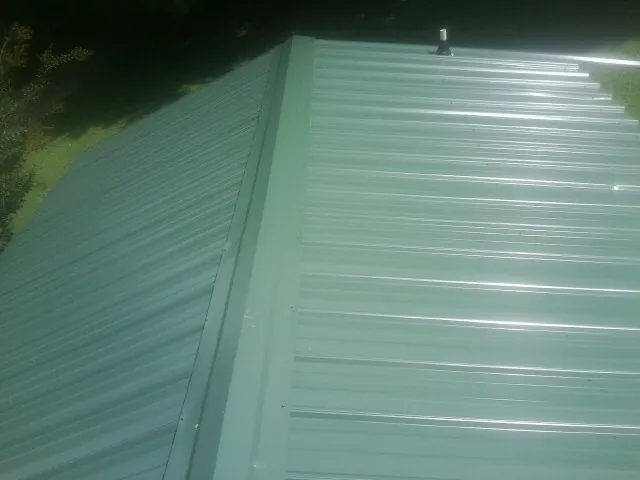 New green metal panels meeting at the ridge of a roof — Flat Roof Repair work by our crew in Hayward