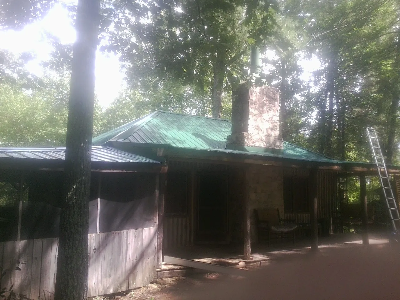 Green metal roof and stone chimney above a log cabin porch in Hayward